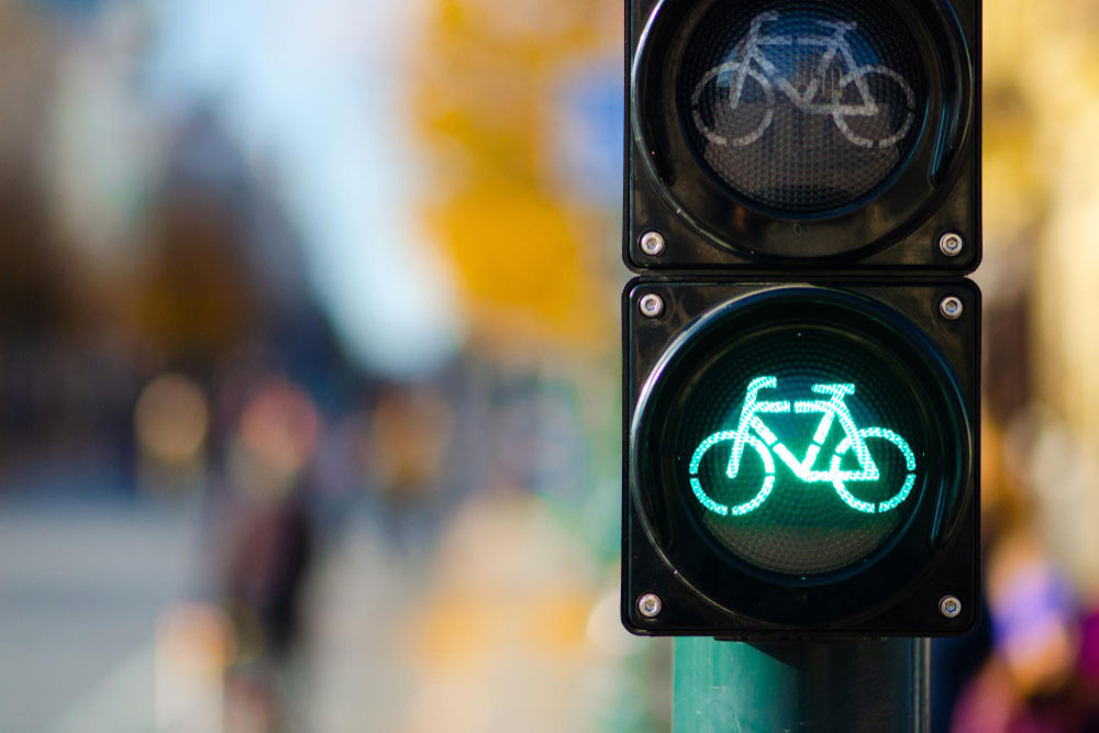 A green traffic light in the shape of a bicycle is lit, while people walk in the background.