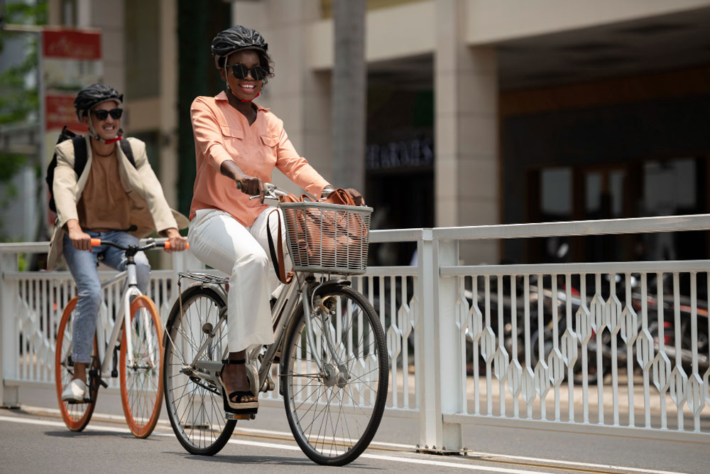 Two smiling people ride bicycles down the street.