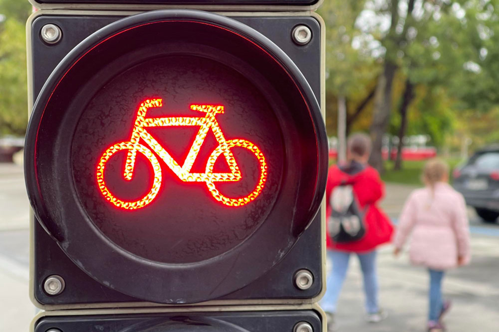 An orange traffic light in the shape of a bicycle is lit, while people walk in the background.